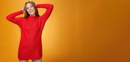 Romantic and sensual cute ginger girlfriend in elegant warm red winter dress holding hands behind head relaxed and carefree smiling delighted tilting head enjoying leisure and holidays photo