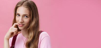 Cute feminine girl learning how make glances and seduce boyfriend with flirty gaze biting finger sensually posing against pink background, flirting making senducing look wearing make-up on date photo