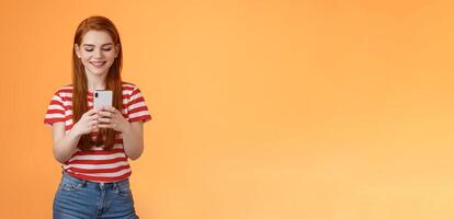 Friendly outgoing modern ginger girl communicating friends, chatting, send funny memes hold smartphone, smiling happy looking gadget display, use social media app enjoy new device feature photo