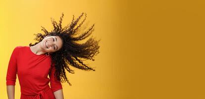 Girl getting carefree and wild waving hair and making sun with curls flying in air smiling broadly tilting head and having fun, dancing delighted and amused feeling playful against yellow background photo