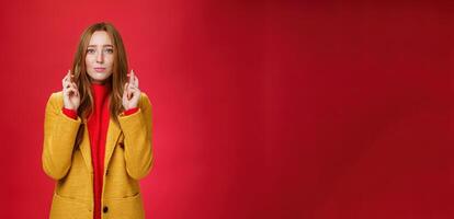 Girl having faith everything be fine cross fingers for good luck as supplicating, making wish looking hopeful at camera anticiapting miracle and dream come true against red background photo