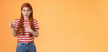 Insecure questioned frustrated cute redhead girl feel nervous unsure about suspicious offer frowning, grimacing doubtful and hesitant, pointing left look camera puzzled, asking question photo