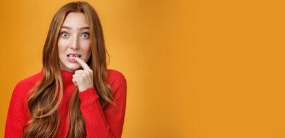Silly, cute redhead woman making innocent oops expression holding finger on lip and looking scared with questioned expression at camera making mistake and trying get away of troubles with flirty gaze photo