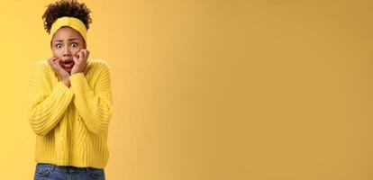 Scared stupefied trembling insecure timid african american woman afraid widen eyes gasping touching face terrified look horror eyes terrified cannot move shaking fear, standing yellow background photo