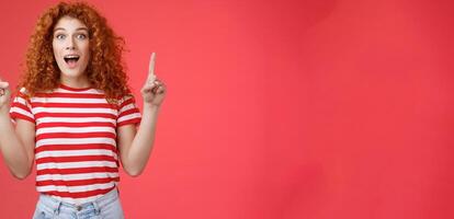 Omg fascinating store check it out. Impressed excited good-looking redhead curly emotive girl drop jaw astonished happy pointing up index fingers directed upwards telling cool news photo