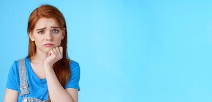Upset worried cute uneasy goomy redhead girl frowning, pull disappointed face, feel pity embarrassed, lean hand whining, complaining, loosing lottery, stand blue background sorrow photo