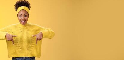 Enthusiastic impressed surprised beautiful african-american woman widen eyes drop jaw smiling gasping astonished pointing down amused standing yellow background showing amazing opportunity photo