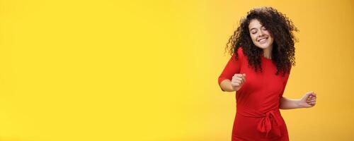 Carefree woman dancing on dance floor with close eyes and smile enjoying life feeling happy and joyful close eyes and making tender expression as moving to rhythm of music over yellow background photo