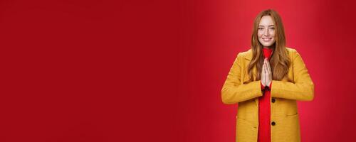 Girl welcomes us with buddhist namaste gesture pressing palms together over chest smiling friendly and delighted with carefree emotions holding hands in pray, posing happily over red background photo