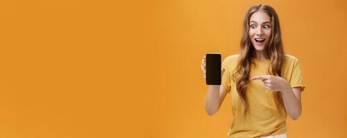 Portrait of excited woman feeling amazed holding awesome new smartphone in hand pointing at cellphone screen popping eyes like crazy at device being charmed with cool technology product photo