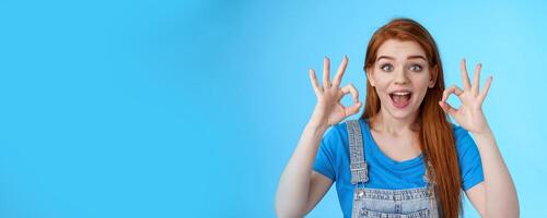 Excellent choice. Redhead female friend approve awesome idea, support accept good purshace, show okay ok confirmation gesture, smiling judging, give positive feedback, stand satisfied blue background photo