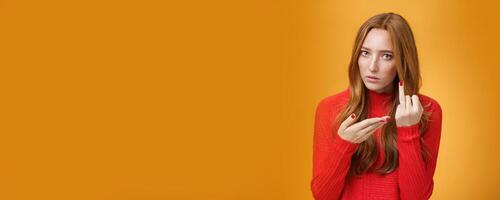 Redhead girl asking where wedding ring being fed up waiting proposal extending finger and pointing at it questioned and pissed having argument with boyfriend over orange background photo
