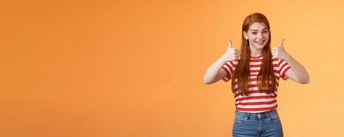Good work, keep going. Girl encourage friend, say well done, show satisfactory sign, thumbs-up and smiling pleased, agree, approve nice choice, accept point view, stand orange background photo