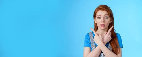 Questioned ambushed cute redhead woman asking advice picking product, cross hands pointing sideways, show left right choices, look camera wondered uncertain, making decision, blue background photo