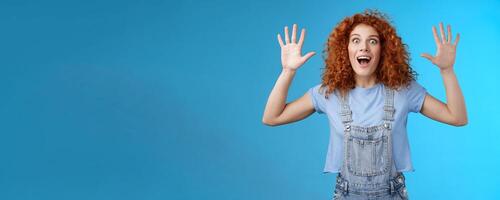 Excited crazy playful funny redhead curly emotive girl yelling carefree raise hands surrender up open mouth fool around smiling broadly stare camera joyful express wild daring emotions photo
