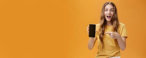 Girl surprised with awesome smartphone features. Portrait of delighted and amazed cute european slender woman with wavy natural hairstyle showing cellphone pointing at gadget screen at app photo