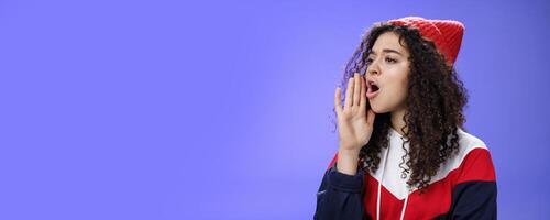 Portrait of worried sister calling sibling outdoors open mouth looking left seriously and holding palm near lips as shouting name searching someone, posing concerned over blue background photo