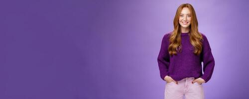 Optimistic attractive ginger girl in 20s wearing purple sweater standing ready and energized over violer background smiling friendly and confident at camera, showing readiness to have fun photo