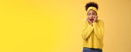 Scared stupefied trembling insecure timid african american woman afraid widen eyes gasping touching face terrified look horror eyes terrified cannot move shaking fear, standing yellow background photo