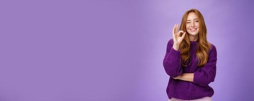 Nice work you did great. Satisfied and happy charming assertive and supportive redhead woman in purple sweater smiling and winking in approval showing okay gesture, liking product over violet wall photo