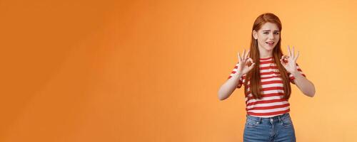 Chill carefree relaxed redhead girl assure everything fine, make okay signs, approval, nothing worry about everything good, stand orange background unbothered, satisfied not bad result photo