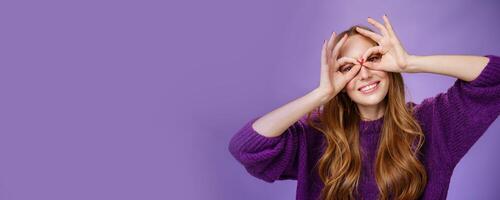 Hey smile more. Portrait of bright and funny charming redhead girl in purple sweater making mask with hands over eyes and smiling broadly acting like superhero posing excited and playful photo