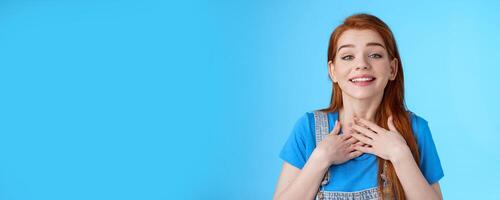 Grateful sincere cute charming redhead female thanking friends, smiling delighted appreciate nice tender gesture, press palms chest heart, grateful, look admiration and love, stand blue background photo