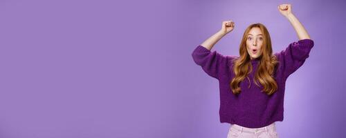 Excited and thrilled woman reacting to unexpected goal raising hands in wave gesture folding lips inhaling breath to scream yes and wow being impressed, triumphing from success and good news photo