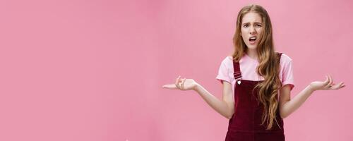 So what, no big deal. Rude and impolite arrogant young girl with high ego in overalls spreading hands sideways in questioned, bothered gesture expressing confusion, feeling pissed with stupid question photo