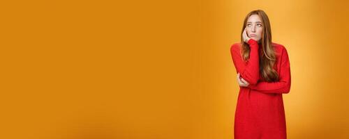 Sorrow and upset lonely woman leaning head on palm in upset pose looking gloomy at upper left corner as remembering unhappy story or being bored standing uneasy over orange wall photo