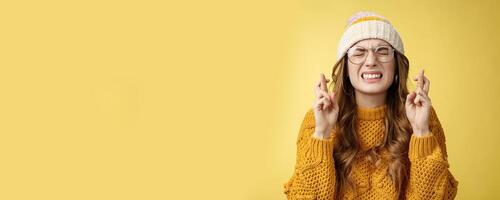Close-up worried extremely nervous cute nerdy girl college student praying put effort dream come true clench teeth close eyes cross fingers good luck make wish standing supplicating yellow background photo