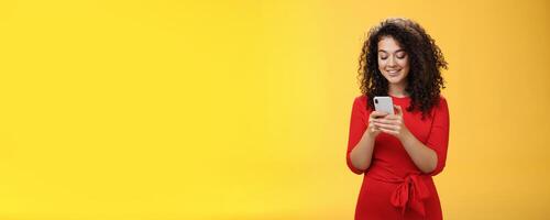 Gil sending message spread news across social network having party inviting friends via smartphone holding mobile phone in hands smiling broadly at device screen as posing over yellow background photo