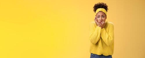 Afraid concerned nervous young african american female employee worried anxious be fired clench teeth stooping touch face insecure bit fingers standing scared terrified, yellow background photo