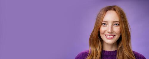 Headshot of charming attractive and happy young redhead woman with freckles and bright white smile, grinning satisfied at camera as posing over purple background friendly and delighted photo