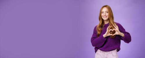 Girl loves new place to hang out, showing heart gesture and smiling satisfied and cute, expressing sympathy and admiration looking romantic and dreamy against purple background photo