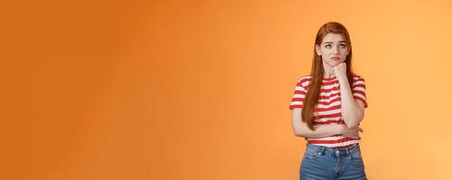 Upset redhead woman losing lottery feel uneasy distressed, look up regret loss, lean on fist pulling sad face, standing lonely unhappy orange background thinking, taking hard decision photo