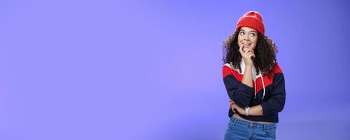 Girl making up idea what snowman built standing cute and silly with thoughtful expression biting finger as thinking, smiling delighted, having interesting thought standing in hat and warm sweatshirt photo
