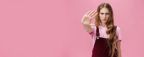 Woman protest against testing products on animals. Serious-looking confident young girl with long wavy hair frowning looking sctrict at camera pulling palm towards camera in prohibition and no gesture photo