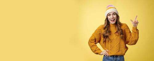 Amused friendly outgoing young girl having fun talking friends amused discussing cool promo pointing upper right corner smiling happily talking casually thrilled look camera, yellow background photo