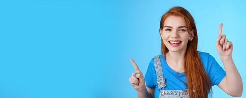 Close-up cheerful carefree redhead dancing girl pointing up, raising fingers, smiling amused, having fun, stand blue background entertained, enjoy music party, disco mood, carefree emotions concept photo