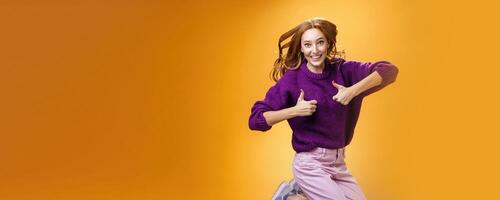 Optimistic and cheerful woman liking promotion lifting thumbs up and jumping from excitement and delighted, having fun recommending good idea smiling thrilled and enthusiastic over orange background photo