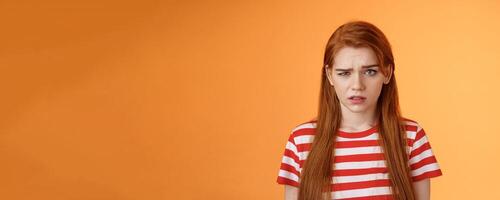 Close-up stupified puzzled redhead perplexed woman, open mouth raise eyebrow full disbelief, confused frowning, cannot understand person saying nonsense, stand questioned orange background photo