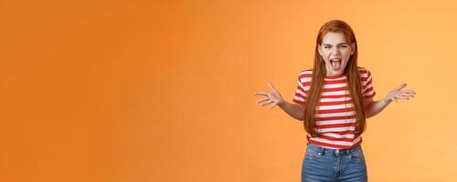 Pissed angry and annoyed redhead female arguing yelling with hatred and anger, spread hands sideways dismay, complain look disappointed upset and hateful, stand orange background photo