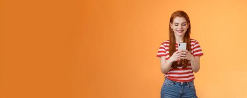 Friendly outgoing modern ginger girl communicating friends, chatting, send funny memes hold smartphone, smiling happy looking gadget display, use social media app enjoy new device feature photo