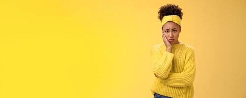 Upset cute gloomy young timid girl offended feel sadness regret touch cheek painful toothache make upset miserable pitty expression, troubled uncertain what do standing insecure yellow background photo