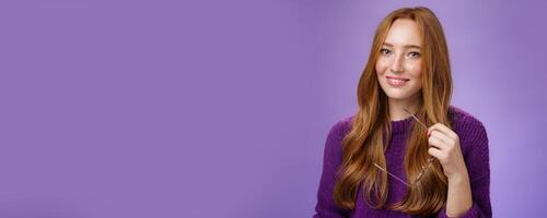 Close-up shot of charming tender and cute redhead woman in purple sweater holding glasses and smiling broadly as having nice friendly conversation against violet background photo