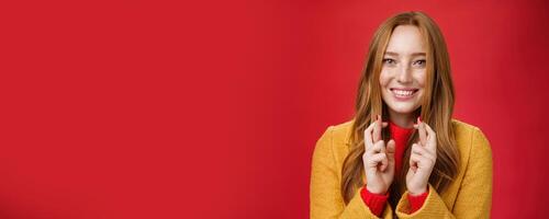 Close-up shot of satisfied happy young 20s woman in yellow coat showing thumbs up gesture in like and approval giving positive feedback enjoying nice event standing over red background, smiling cute photo