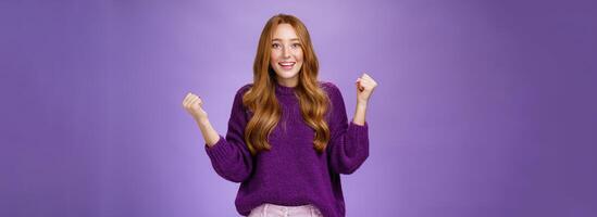 Girl proud of herself making successful effort clenching raised fists in celebration and triumph smiling broadly with surprised and relieved expression, winning, achieving goal over purple background photo