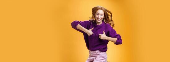 Optimistic and cheerful woman liking promotion lifting thumbs up and jumping from excitement and delighted, having fun recommending good idea smiling thrilled and enthusiastic over orange background photo