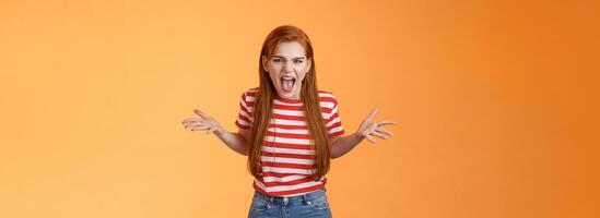 Pissed angry and annoyed redhead female arguing yelling with hatred and anger, spread hands sideways dismay, complain look disappointed upset and hateful, stand orange background photo